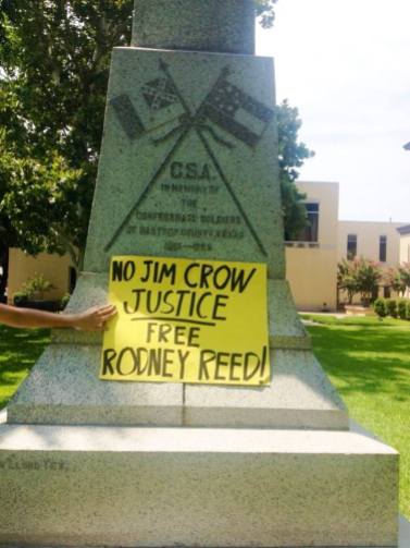 A supporter holds a sign saying "No Jim Crow Justice" in front of a Confederate monument at the Bastrop Co. Courthouse
